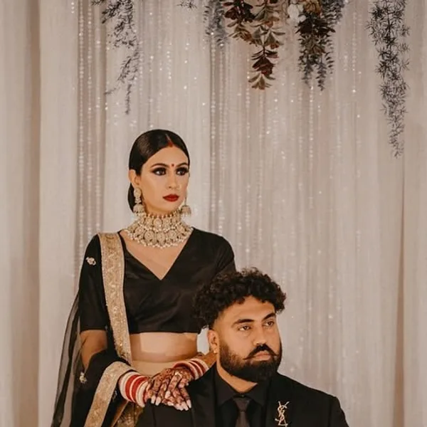 A groom in an all-black suit, seated beside his bride