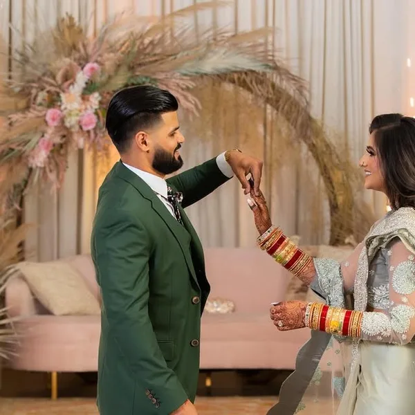 A groom in a forest-green suit with his bride at their reception